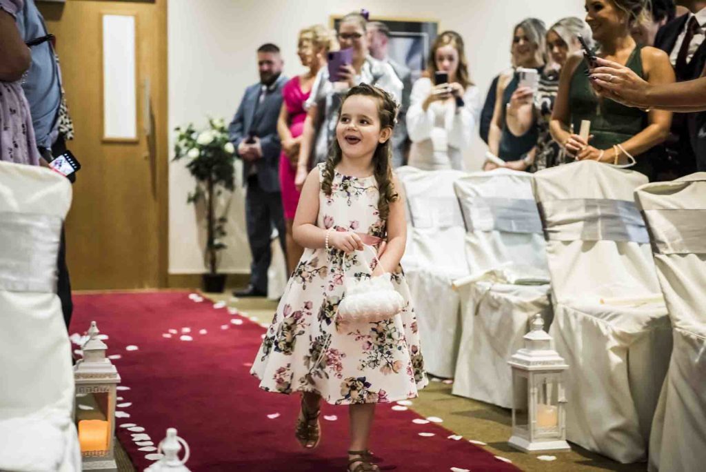 Adorable flower girl scattering petals along the aisle with a big smile.